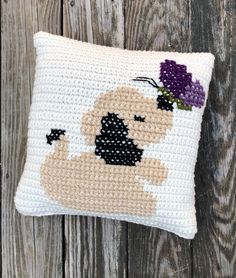 a crocheted pillow with a dog and flowers on it sitting on a wooden surface