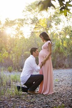 a man kneeling down next to a pregnant woman in a pink dress and white shirt