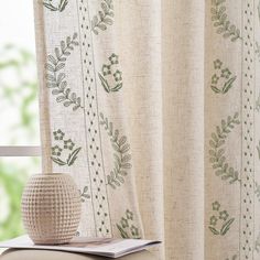 a white vase sitting on top of a table next to a window sill with curtains