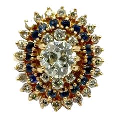 This ring showcases the exceptional craftsmanship and attention to detail characteristic of early 20th-century jewelry. The ring features a dazzling combination of Old European cut diamonds and sapphires. Old European cut diamonds were popular during the early 20th century and are known for their romantic and vintage appeal, characterized by large facets and a distinctive sparkle. The sapphires add a rich, velvety blue hue to the ring, creating a striking contrast with the brilliance of the diamonds. The center Old European cut diamond weighs apprxoximately 1.65 carats and is surrounded in a step down fashion with another 30 diamonds (weighing approximately 1.00 CTW) and blue sapphires. The diamonds are graded K color and VS clarity. The ring measures 20 x 22mm on top and is currently size Yellow Gold Cocktail Ring, Gold Cocktail Ring, Gold Cocktail, European Cut Diamonds, Cocktail Ring, Blue Hues, Cocktail Rings, Blue Sapphire, Fashion Rings