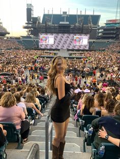 a woman standing in front of a large crowd at a concert with her legs crossed