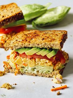 a sandwich with lettuce, tomato and avocado cut in half on a white surface