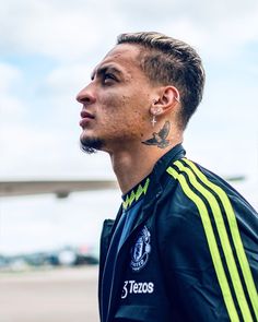 a man with tattoos on his face standing in front of an airport tarmac and looking off into the distance