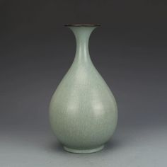 a light green vase sitting on top of a gray table next to a white wall