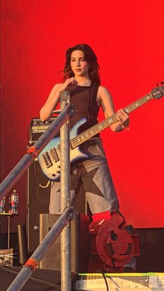 a woman with a guitar standing on top of a metal pole in front of a red wall