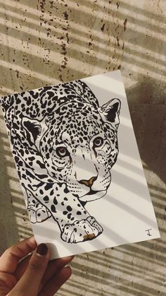 a hand holding up a piece of paper with a drawing of a leopard on it