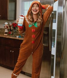 a woman in a christmas costume standing next to a refrigerator holding a drink and smiling