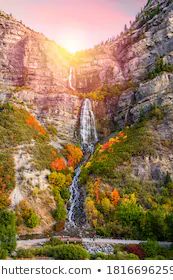 an image of a waterfall in the mountains with fall foliage around it and trees on both sides