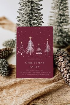 a christmas party card with pine cones and fir trees in the background, on top of a table