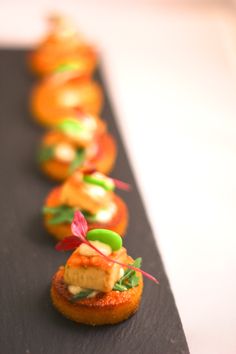 a long line of small cakes with toppings on them sitting on a black plate