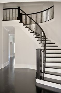 a black and white photo of a spiral staircase in a large room with hardwood floors