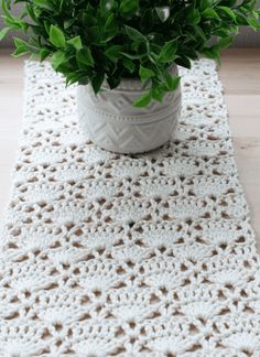 a crocheted table runner with a potted plant in it on a wooden floor