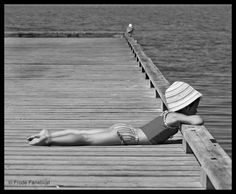 a woman laying on top of a wooden pier next to the ocean wearing a hat