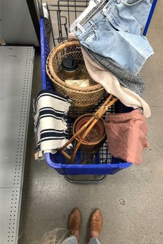 a person standing next to a shopping cart filled with clothes and other items in it