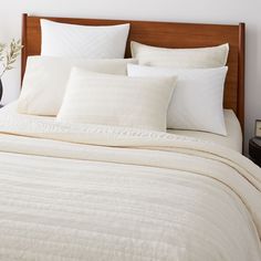 a bed with white sheets and pillows on top of it next to a night stand