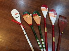 five wooden spoons decorated with santa and snowmen on top of a wood table