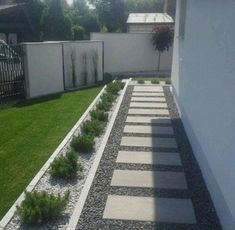 an empty backyard with grass and plants on the side of the house, next to a white fence