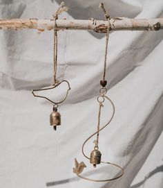 two metal bells hanging from a tree branch with wire and beads attached to the hooks