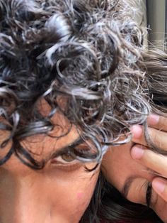 a man with curly hair holding his head to his ear