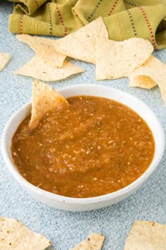 a white bowl filled with salsa and tortilla chips on top of a blue surface