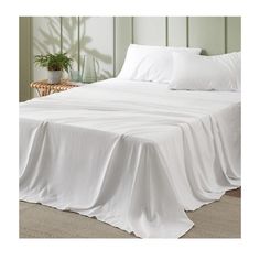 a bed with white sheets and pillows in a room next to a plant on the floor