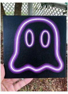 a hand holding up a black and purple sticker with a ghost face on it