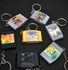 six gameboy keychains are arranged on a black surface, with various games in the background