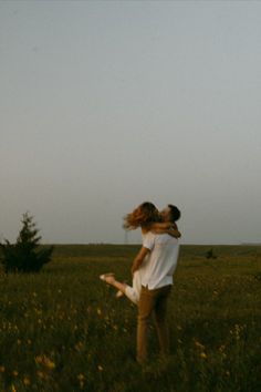 two people in a field with one holding the other up to his head and flying a kite