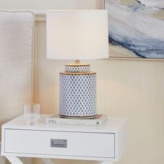 a table with a lamp on top of it next to a white chair and painting