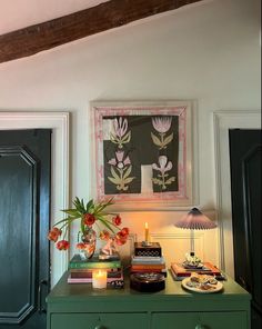 a green dresser topped with lots of books next to a painting on the wall above it