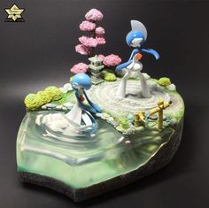 two figurines standing on top of a rock in the middle of a pond