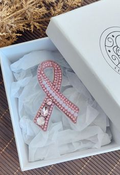 an open box with a pink ribbon on it and some flowers in the back ground