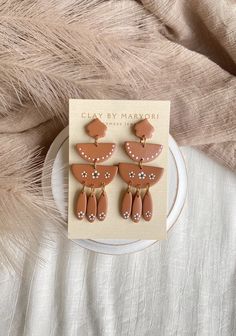 two pairs of earrings on top of a white plate next to a feathery background