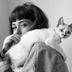 a woman holding a cat in her arms and looking at the camera while wearing a jean jacket