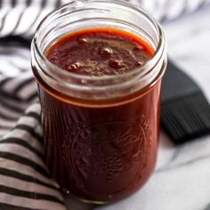 a jar filled with red sauce sitting on top of a striped cloth next to a brush