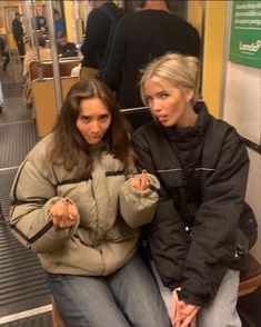 two women sitting on a subway train and one is pointing at the camera with her finger