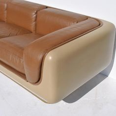 a tan leather couch sitting on top of a white floor next to a wooden table