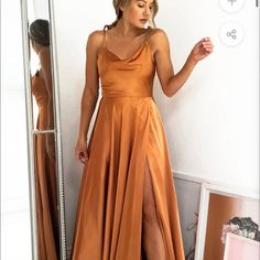 a woman standing in front of a mirror wearing an orange dress with high slits