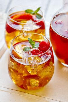 three glasses filled with liquid and fruit on top of a white table next to each other