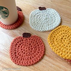 three crocheted coasters sitting on top of a table next to a coffee cup