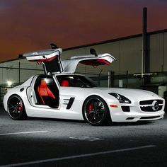 a white sports car with its doors open in front of a fenced area at night