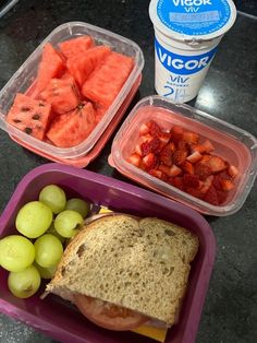 two plastic containers filled with food next to grapes and watermelon