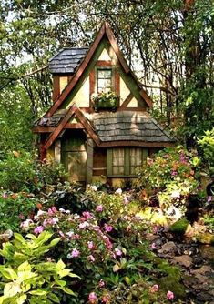 a small house in the middle of some trees and bushes with flowers growing around it