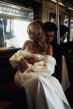 a woman in a white dress sitting on a train next to a man wearing a suit