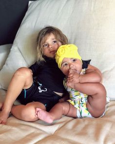 two young children laying on top of a bed next to each other, one holding the baby's head