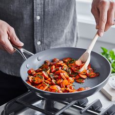 a person cooking food in a frying pan on top of a stove with a wooden spoon