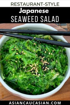 a white bowl filled with greens and chopsticks on top of a wooden table