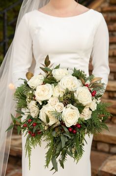 a bride holding a bouquet of white roses and greenery