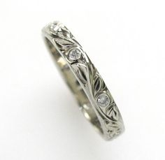 a white gold wedding ring with diamonds on the side and vine design in the middle