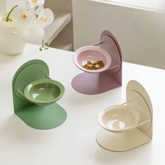 three bowls and two plates on a white table with flowers in the vase behind them